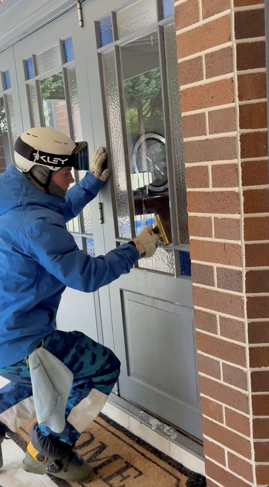 Hugh in full ski gear cleaning a front door